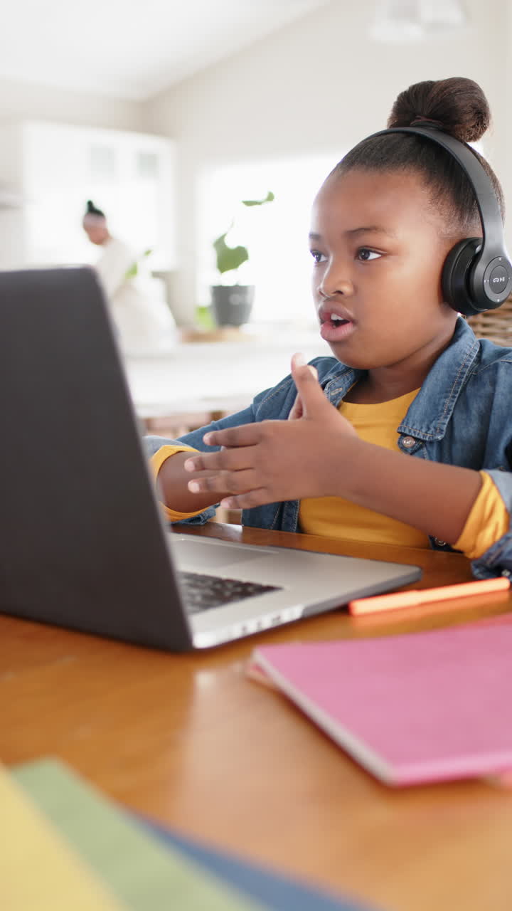 Vertical video of happy african american girl using laptop for online lesson, in slow motion