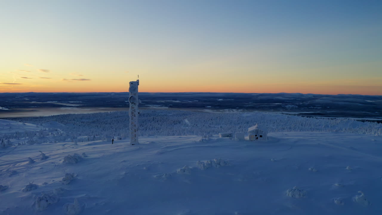 Aerial view orbiting snow covered Lapland remote cabin and communications tower overlooking polar wilderness at sunrise