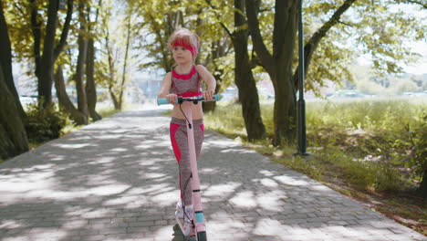 Young-athletic-fit-blonde-girl-rides-traveling-on-electric-scooter-on-road-in-park-on-sunny-day