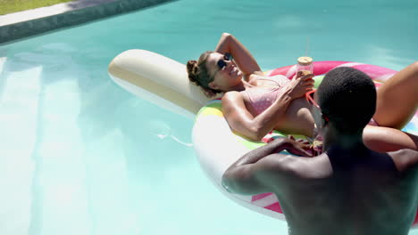 relaxing on pool float, woman sunbathing while african american man holding drink in pool, copy spac