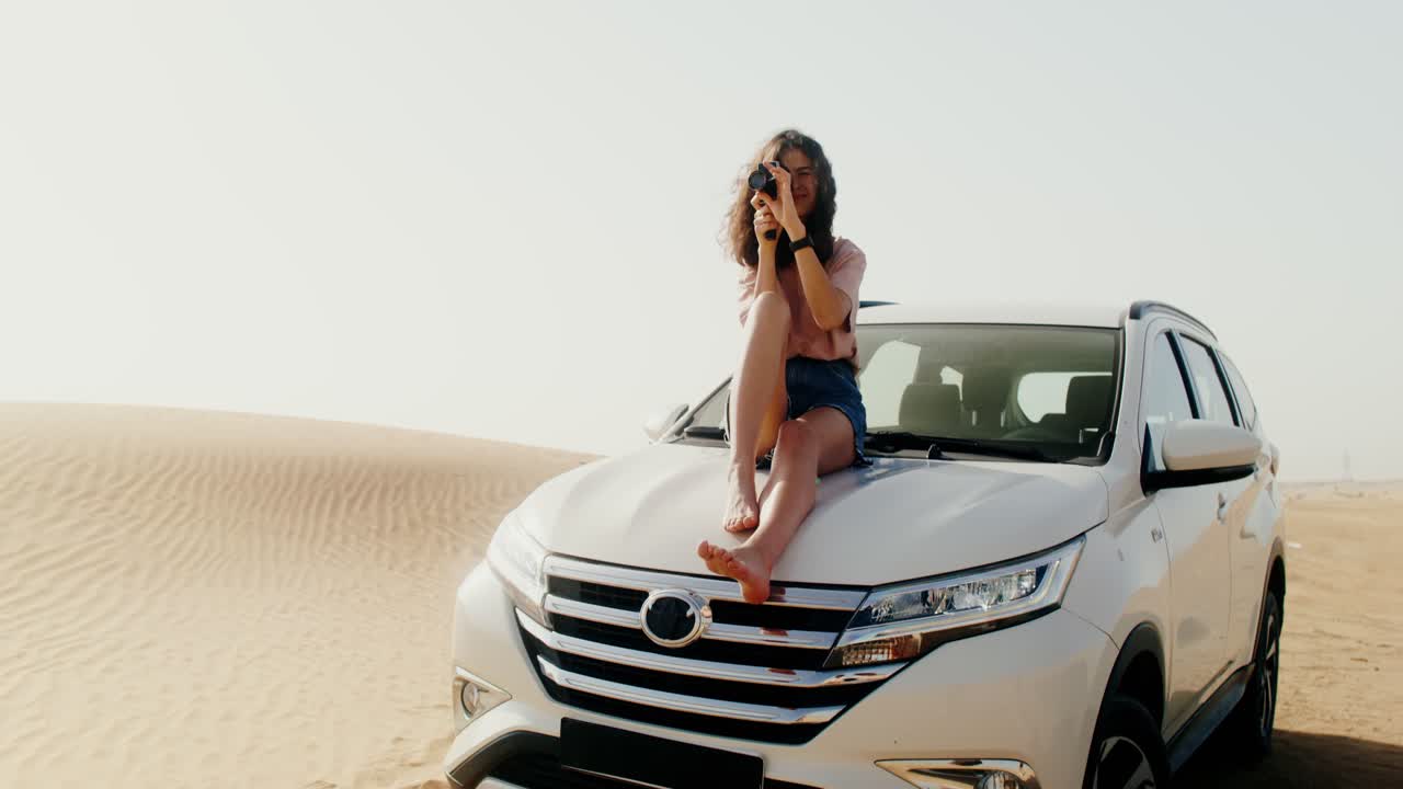 mujer tomando fotos en un capó de coche en el desierto