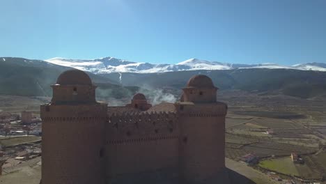 drone close shot of the castle of la calahorra with sierra nevada behind during the winter