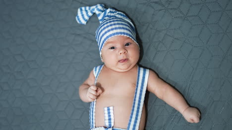 sweet boy wearing striped suit lies on the bed with his hands sideways. funny costume on a kid at the grey background.