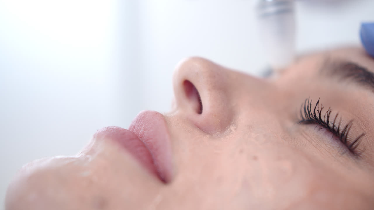 Beautiful slow motion close-up shot of a beautiful young woman's face as she receives a dermatological beauty treatment with a special anti-wrinkle massager in a clinic.