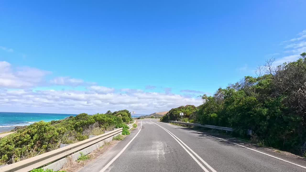A serene drive along the Great Ocean Road with lush greenery, ocean views, and clear blue skies