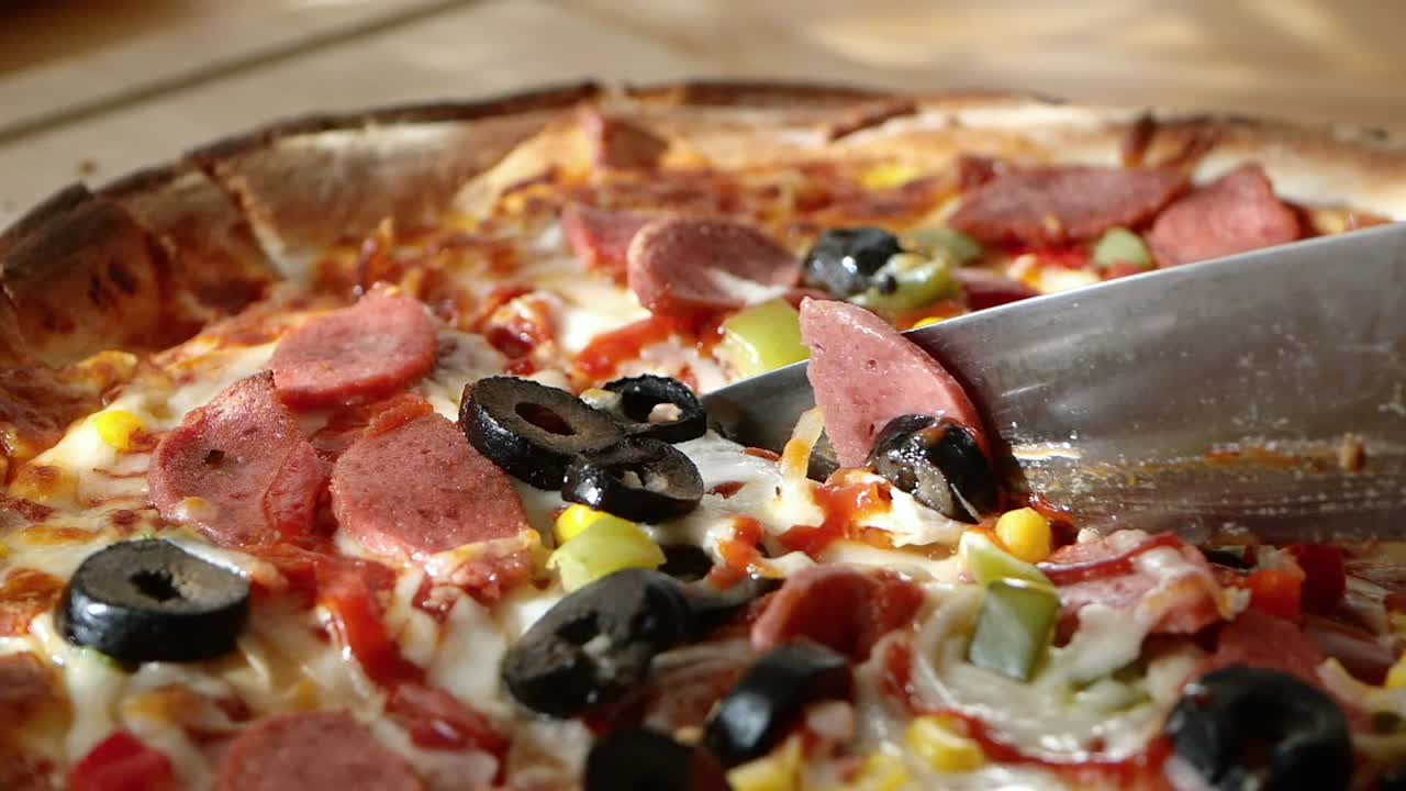 Mano che taglia una pizza appena sfornata con salame e condimenti