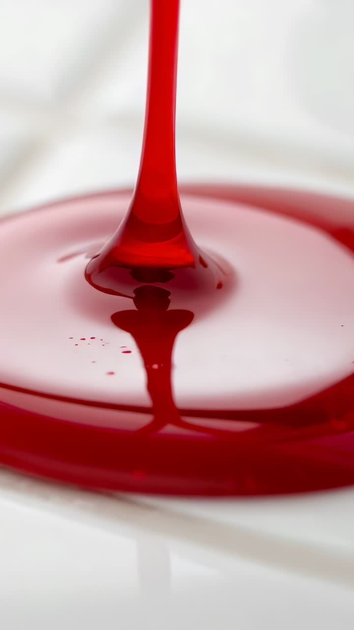 Vertical video: Descending red liquid forming glossy puddle on white ...