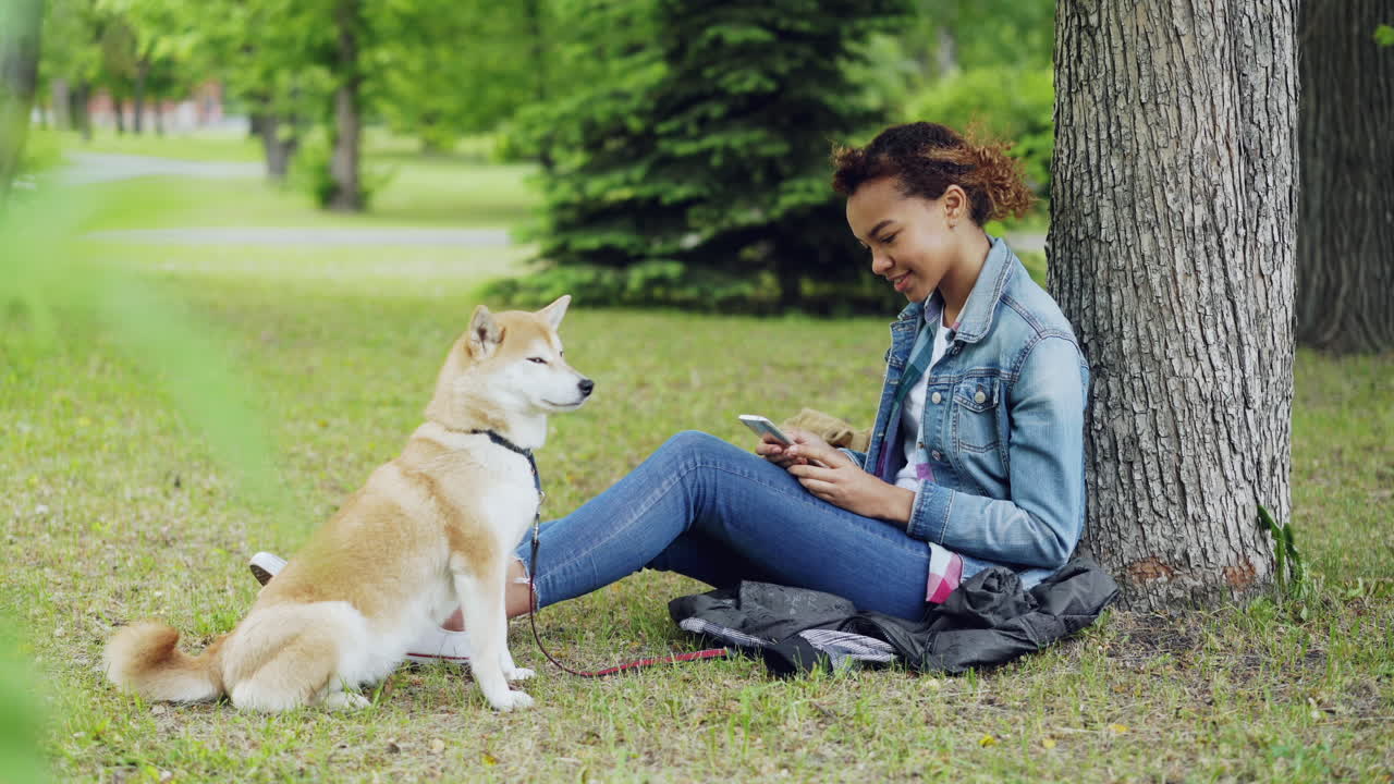 Teenager sitting in a park with her dog, using her smartphone