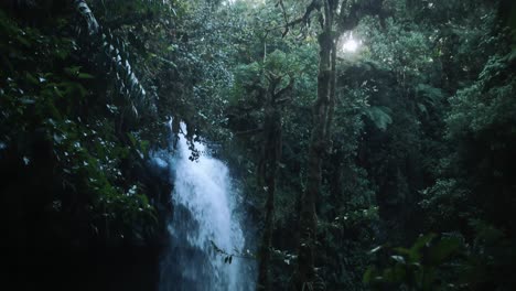 Tilt-down-of-a-waterfall-and-the-sun-shines-through-the-trees-in-a-rainforest