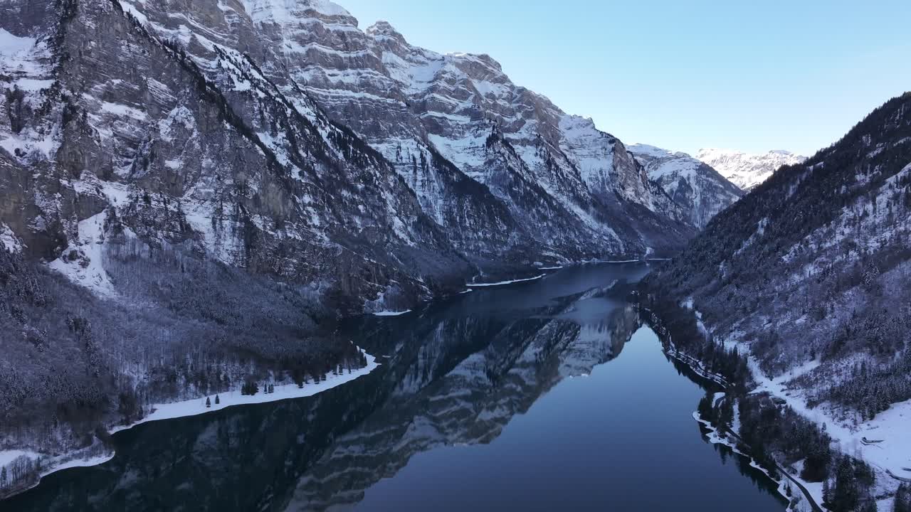 Aerial view of the Klöntalersee in Switzerland. The lake stretches out like a ribbon between towering, snow-capped mountains, creating a breathtaking alpine vista. The reflection of the mountains.