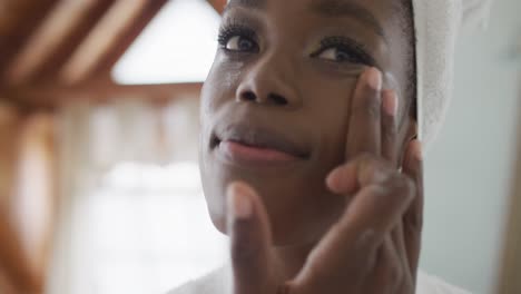 Portrait-of-african-american-attractive-woman-applying-face-cream-in-bathroom