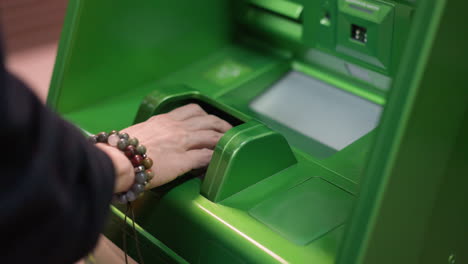 view of a hand wearing beaded bracelets and a black shirt typing a pin at a green atm machine. shot with a handheld camera, capturing the moment of entering banking information