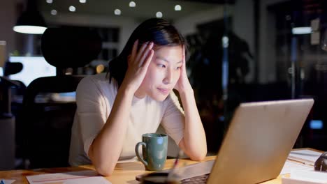 Fokussierte-Asiatische-Gelegenheitsgeschäftsfrau-Mit-Kaffee-Und-Laptop-Nachts-Im-Büro,-Zeitlupe