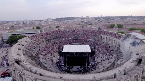 Drone-advance-over-the-Arena-of-Nimes-at-sunset,-people-are-waiting-for-the-stromae-concert