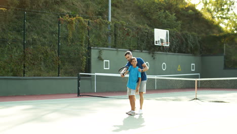 man teaching his teen son how to play tennis on a summer day