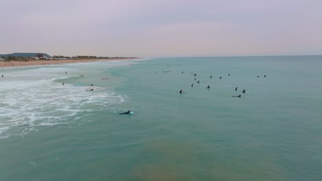 Surfer-Paddeln-In-Neoprenanzügen-Hinaus,-Um-Bei-Sonnenuntergang-über-Das-Türkisfarbene-Wasser-Zu-Brechen