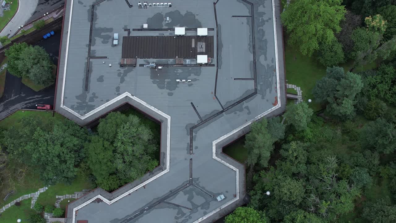 Top-down drone shot of Olivetti’s historic company canteen in Ivrea, designed to harmonize with nature, surrounded by dense forest, example of humane modernist industrial architecture, , slow motion