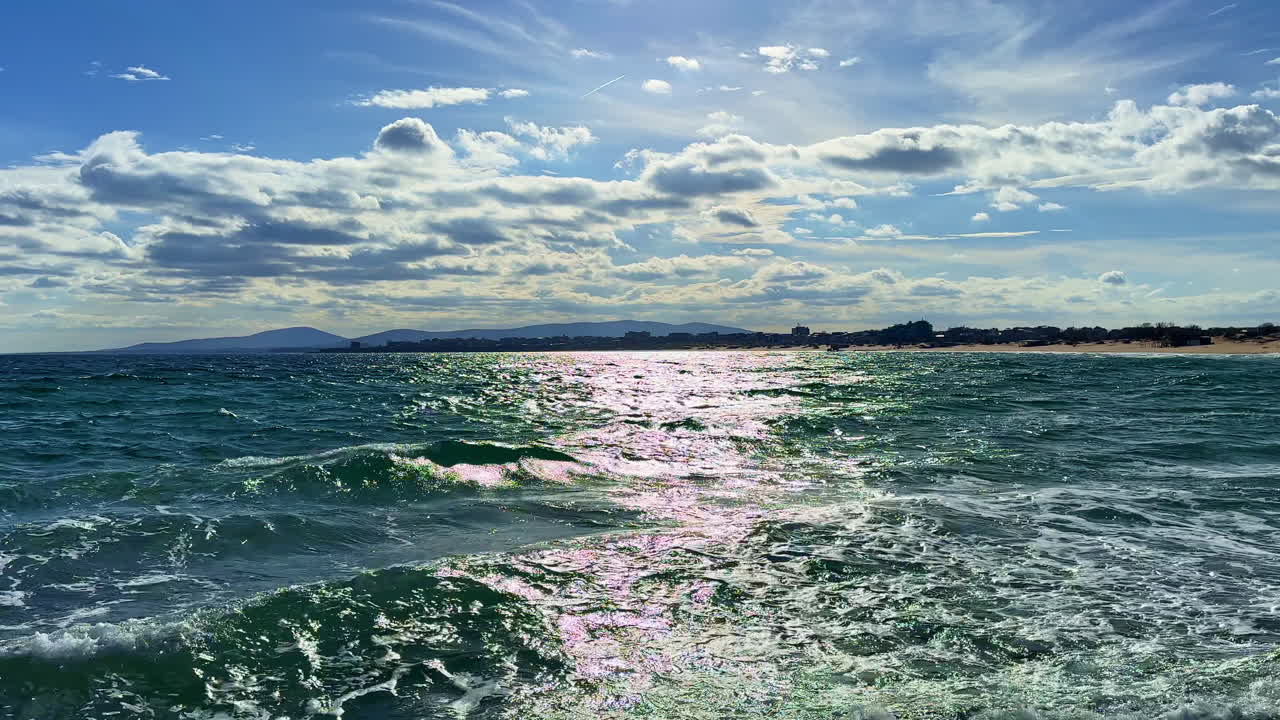 Onde si infrangono sulla riva mentre le nuvole fluttuano nel cielo vicino alla spiaggia a mezzogiorno.