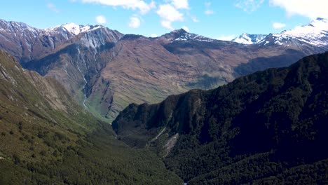 drone view of valley, snow covered peaks and forest on a sunny day in mount aspiring national park, wanaka, new zealand.