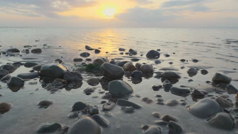 Glistening-pebbles-on-shoreline-with-calm-sea-lapping-during-sunset-in-slow-motion-at-Fleetwood,-Lancashire,-UK