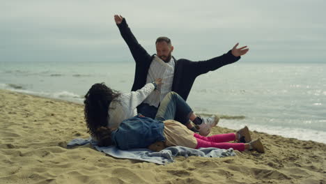 family play tickle beach. mom dad child hugging lying on sea shore sand picnic.