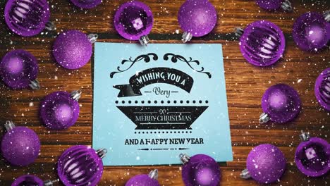 falling snow and merry christmas text note and bauble decorations on wood