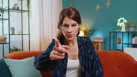 furious young caucasian woman angrily pointing at you through the camera displeased and fuming