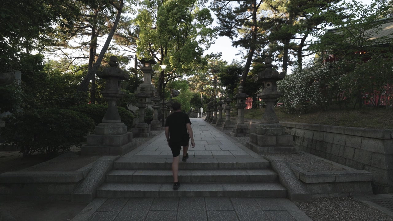 Người đàn ông đi bộ giữa các hokora trên lối đi tại đền thờ ở Osaka, Nhật Bản