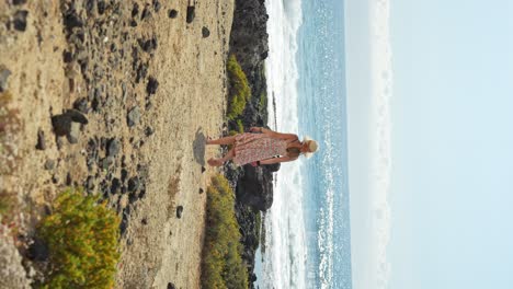 mujer aventurera caminando hacia el océano en tenerife, vista vertical de atrás