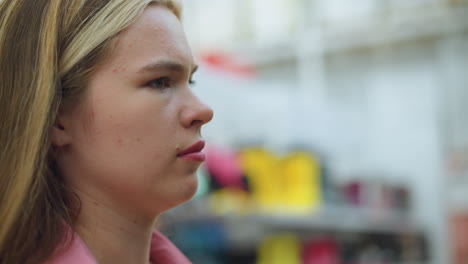 lady in pink dress in store focuses with a disapproving look on an unseen item, background slightly blurred with various colorful items and shelves visible, brightly lit environment