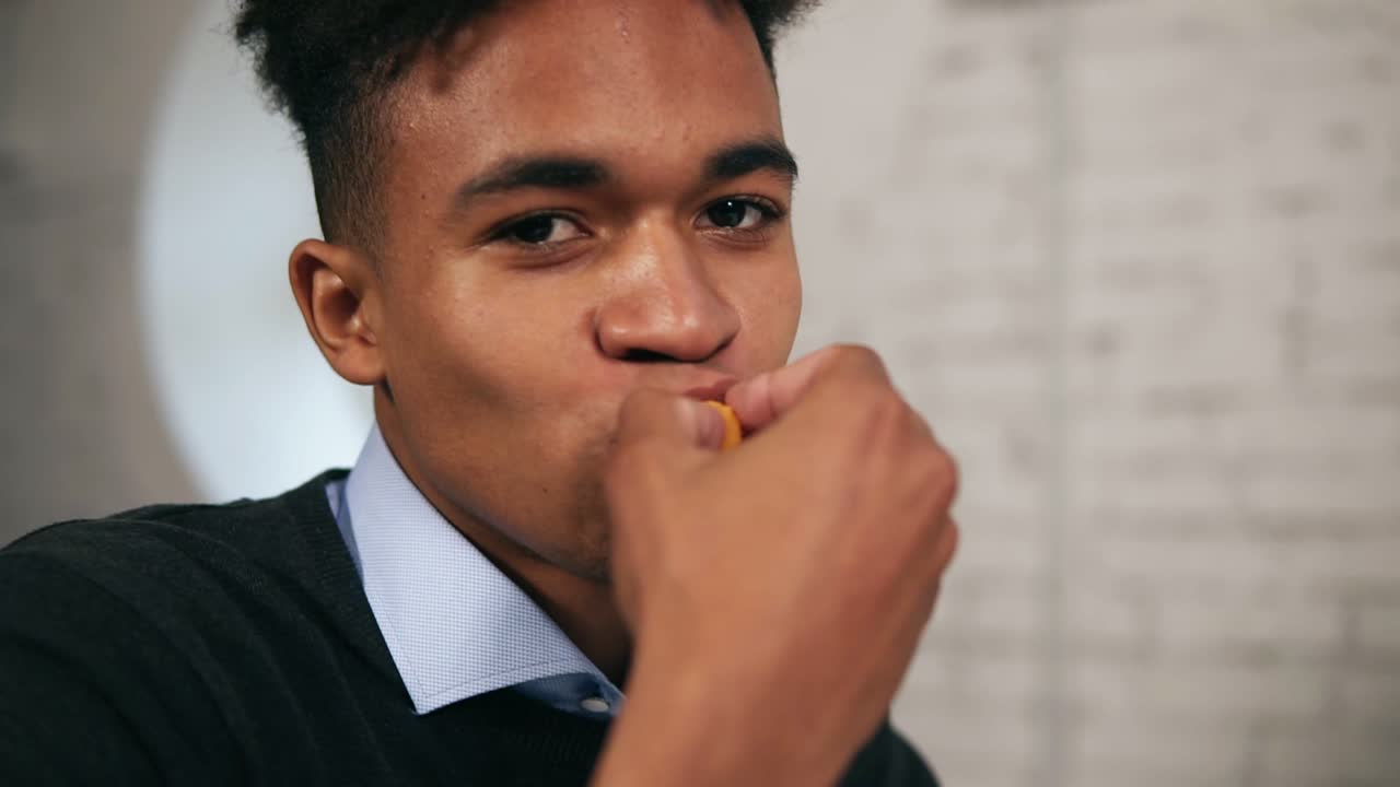 Close Up view of young african american dips chicken nugget in sauce and eats it looking in the camera during lunch at work in