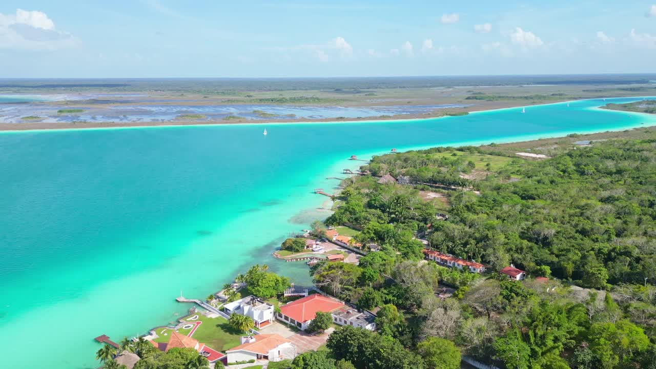 Bacalar lagoon view, turquoise waters meeting green trees and homes along the shore
