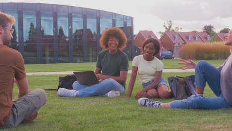 group of university or college students sit on grass outdoors on campus talking and working