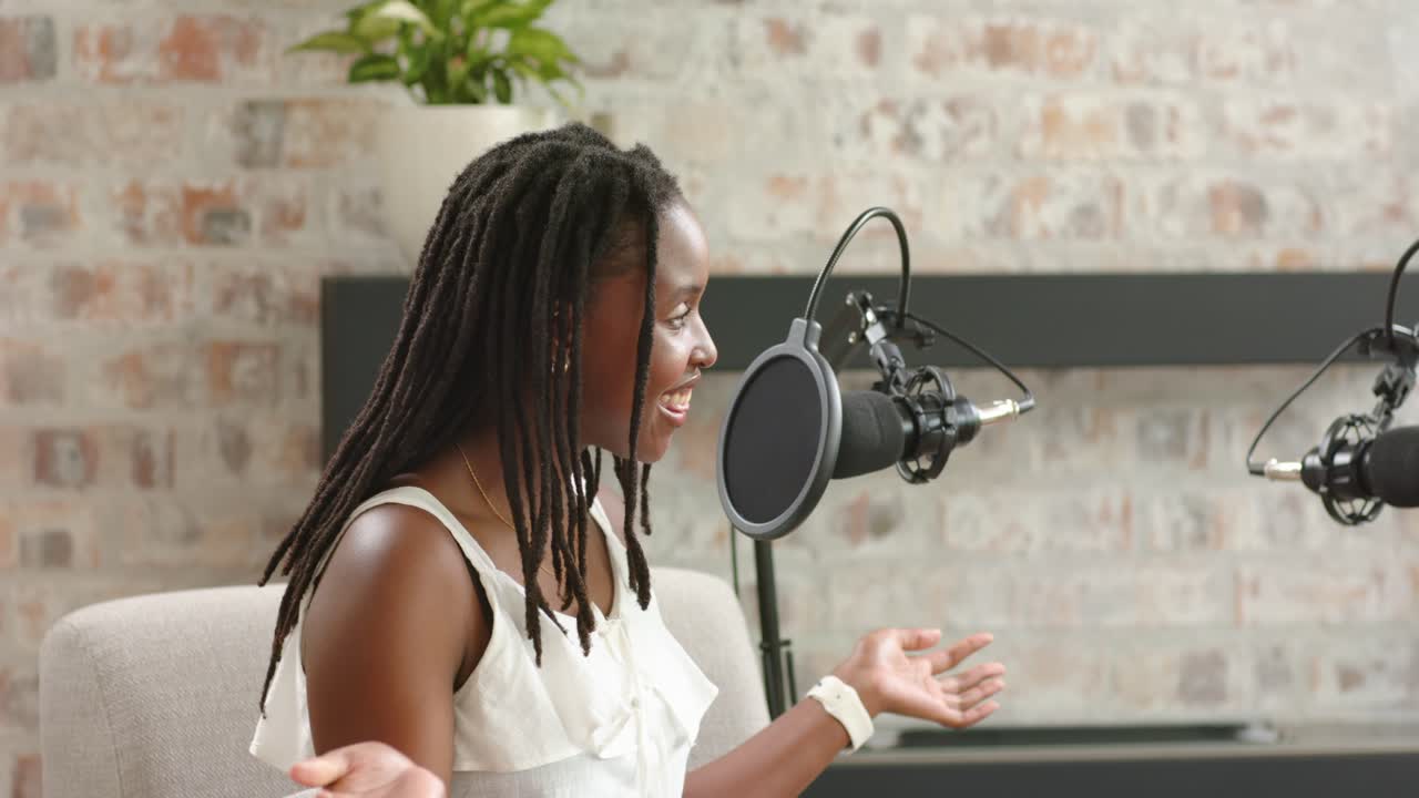Afroamerikanske kvinder, efter mikrofonsignal, taler ind i boom-mikrofoner med popfiltre og podcaster i et studie.