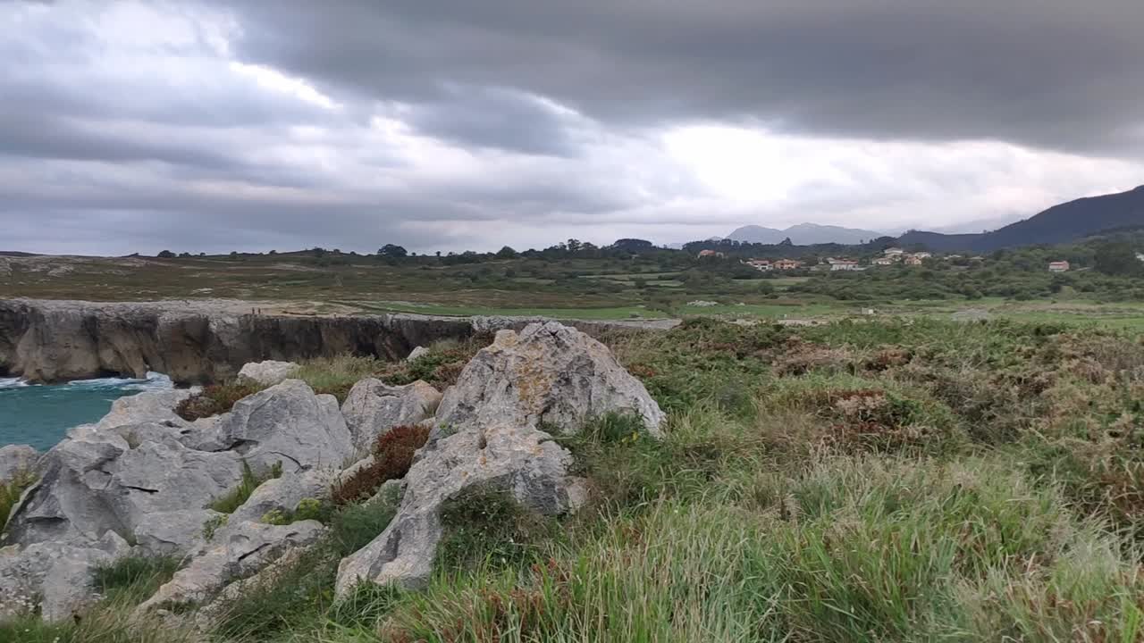 Cliffside view of Guadamia, Asturias, with rocks, grass, and dramatic cloudy sky