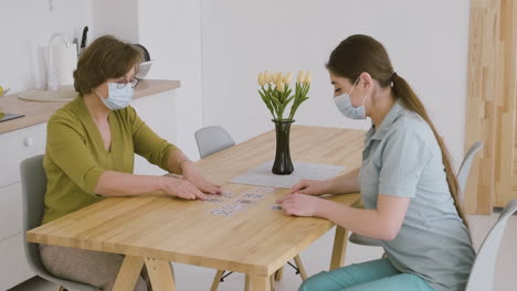 Mujer-Mayor-Y-Doctora-Con-Máscara-Facial-Jugando-A-Las-Cartas-En-La-Mesa