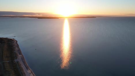 sunrise hyperlapse as light rises and spreads across calm ocean and coastline, aerial