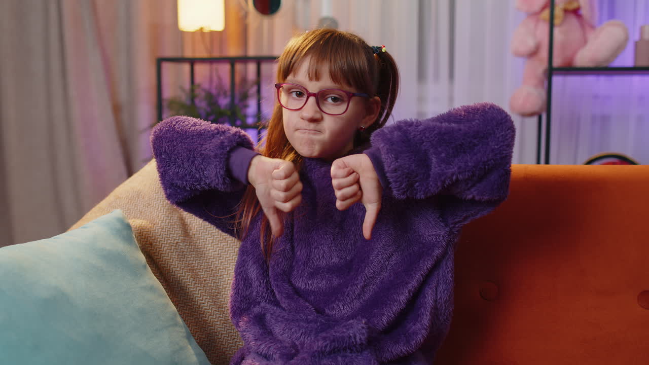 Upset teen girl showing thumbs down, dislike bad work, disapproval, dissatisfied feedback at home