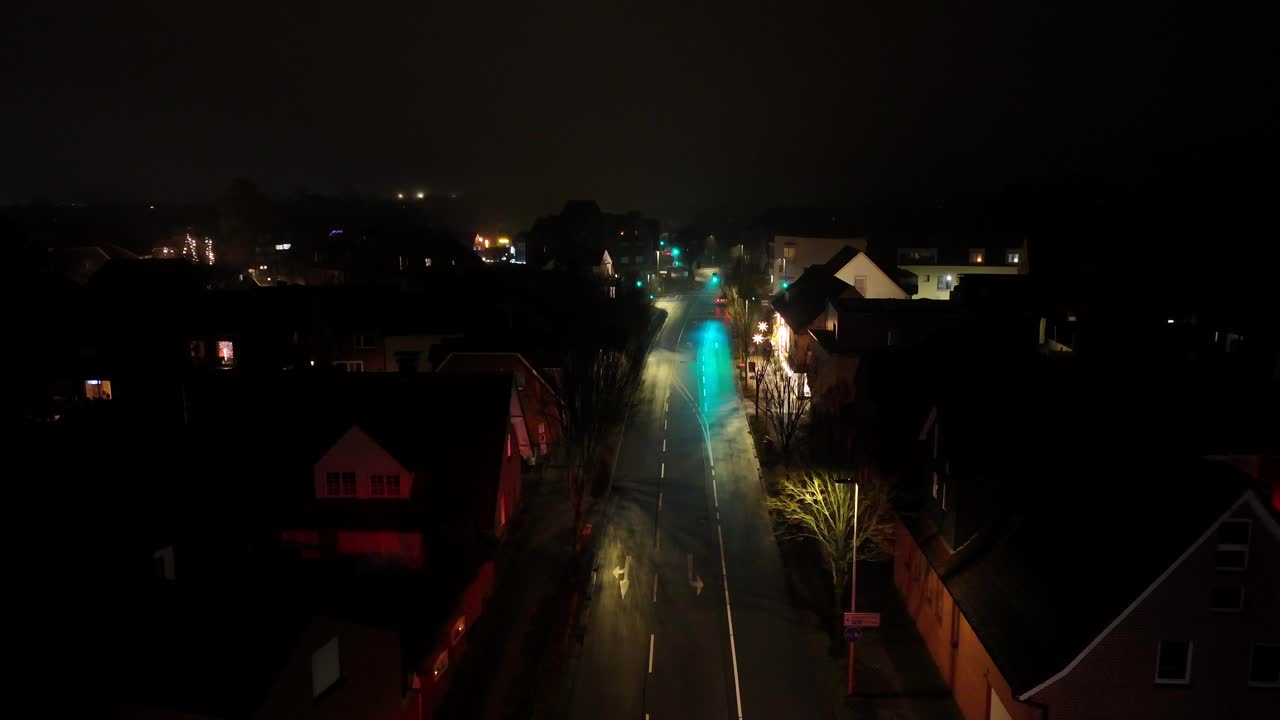Car on Main Street of American neighborhood a night. Rainy winter day in Christmas season. Houses and homes along road. Drone wide shot at midnight. Quiet suburban housing in USA.