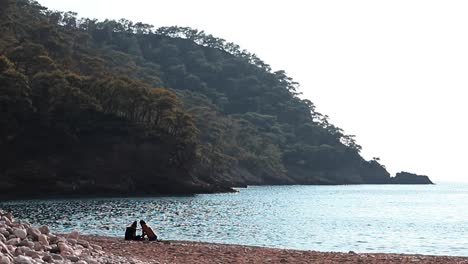a couple sitting on the beach sand, coast side of turkey