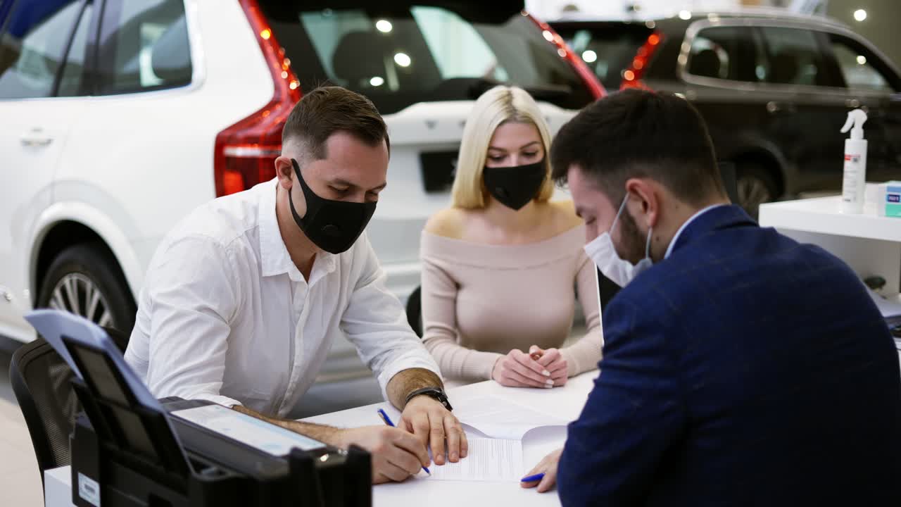 pareja en máscaras compra de un coche nuevo, firmar el contrato en la sala de exposición