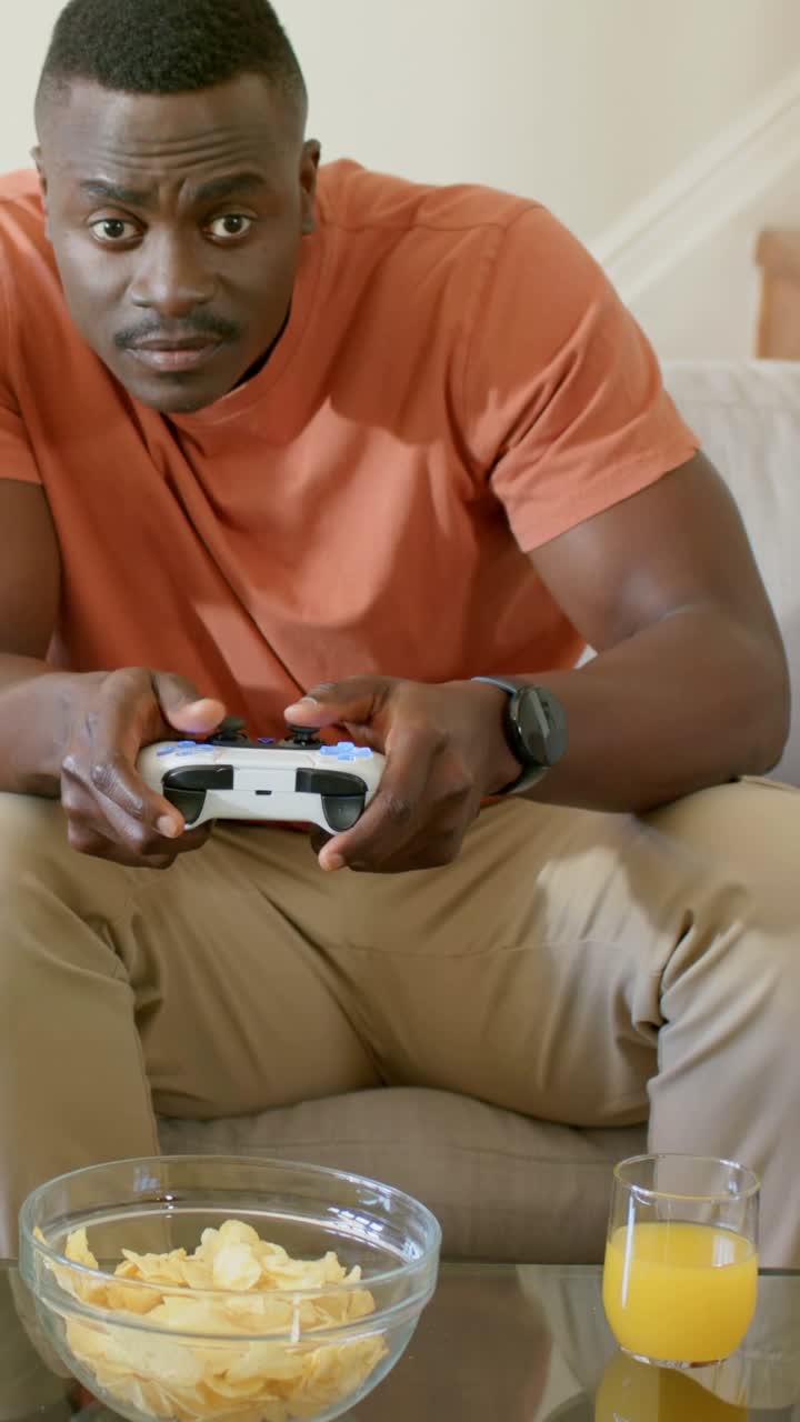 Vertical video: Reacting guy moving pad grip with game updating on couch, orange tee, chips, juice