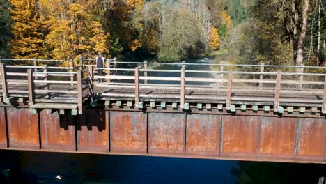 low angle revealing drone shot of lady looking at view on old wooden rail bridge in canada in the fall