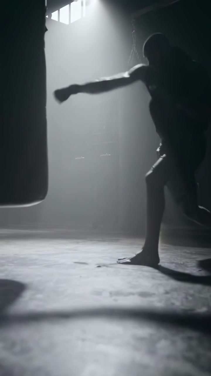 Pugile professionista che si allena con il sacco da boxe in una palestra buia