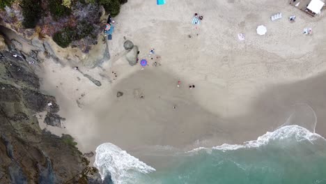 top-down shot of waves and rocks on laguna beach and tilt up towards a huge beachside resort with a pool