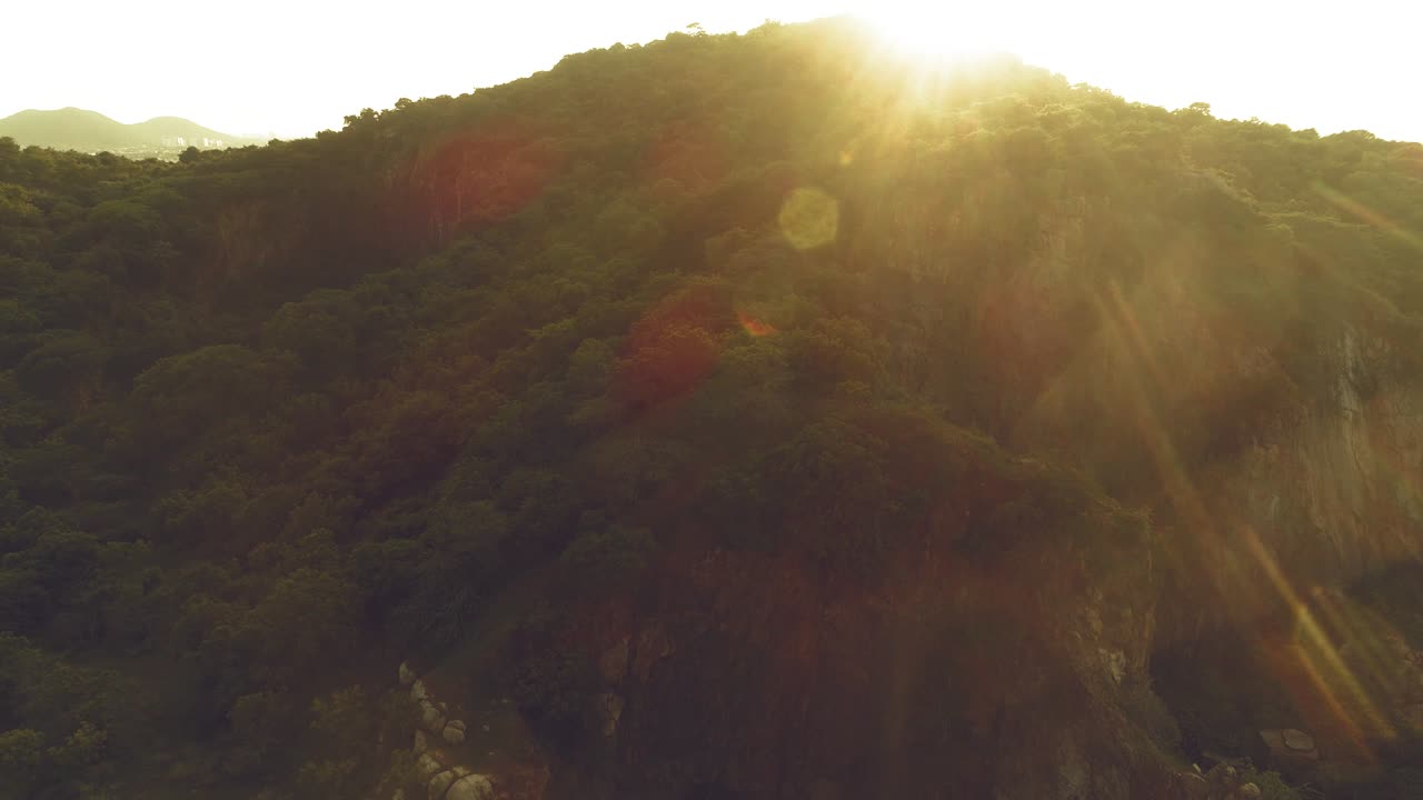 산꼭대기에서 나오는 태양 플레어를 보여주는 산 아래로 이동하는 드론 샷