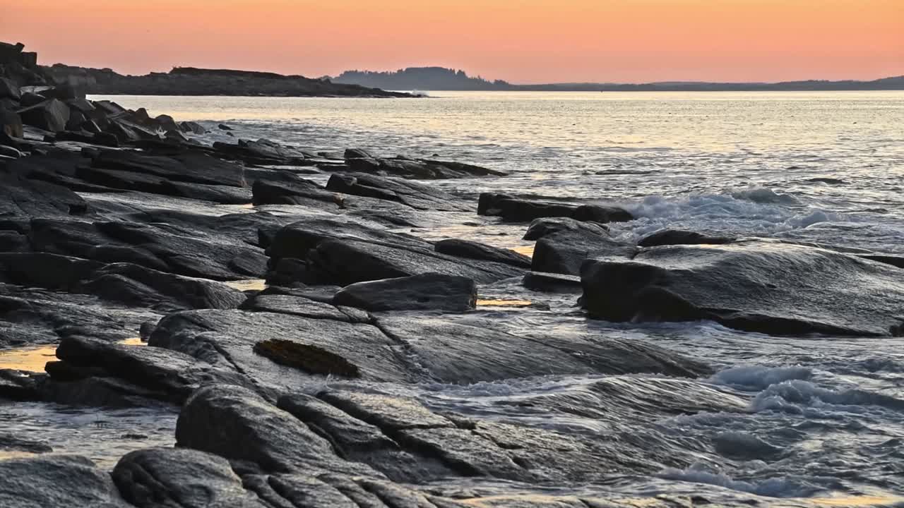Blue sea waves glide over the rocks at sunset