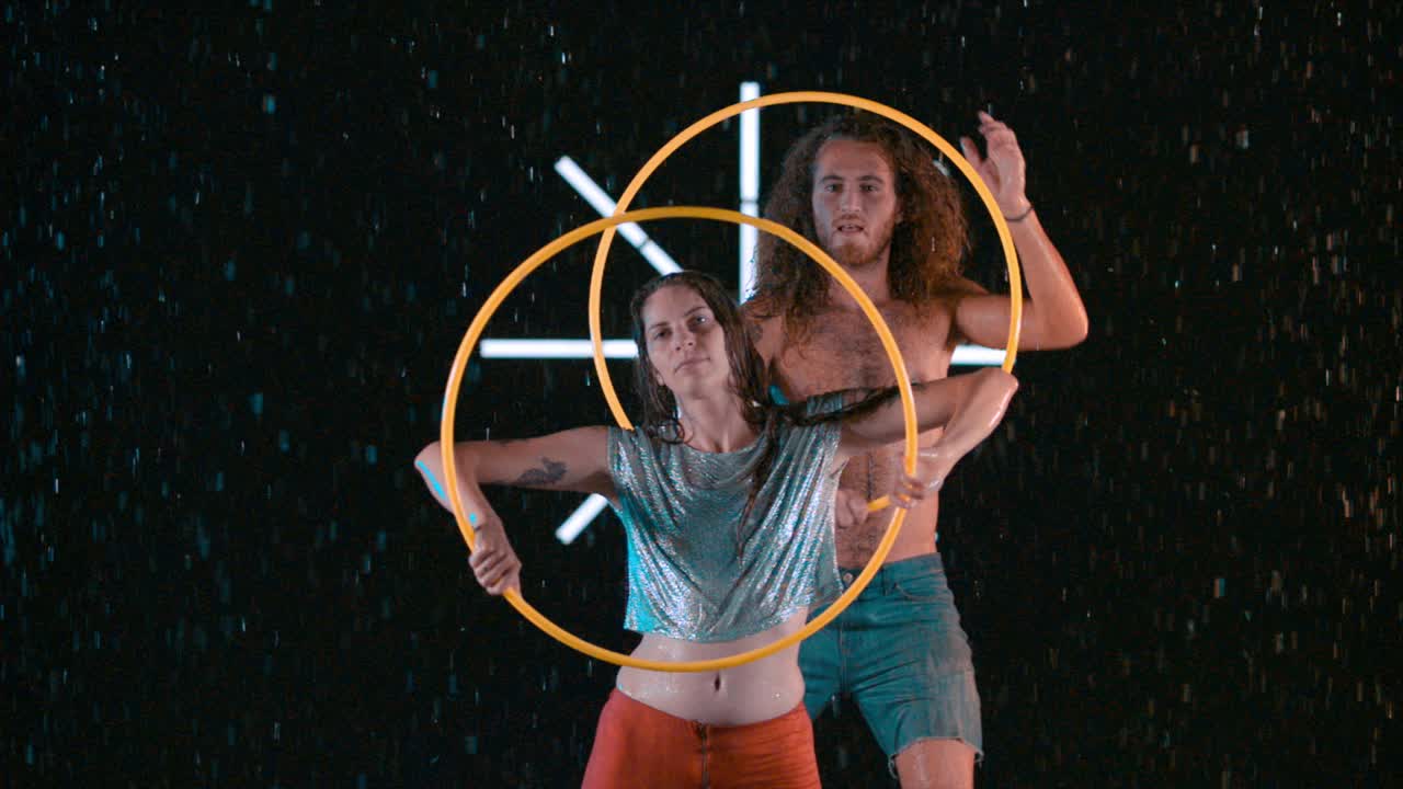 Male and female hula hoopers performing artistic visual effects in wet studio