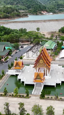 drone footage captures a serene buddhist temple in phuket, thailand, surrounded by lush greenery and tranquil water bodies