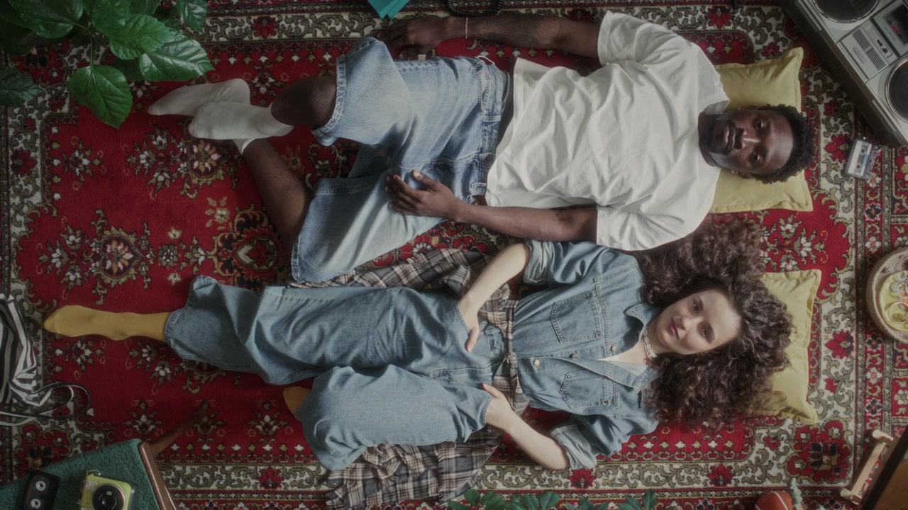 Top View of Diverse Young Couple Lying on Red Vintage Rug and Posing for Camera